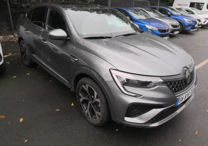 Renault Arkana gris métal foncé vu en 3/4 avant droit, avec jantes alliage et toit ouvrant électrique visible.
