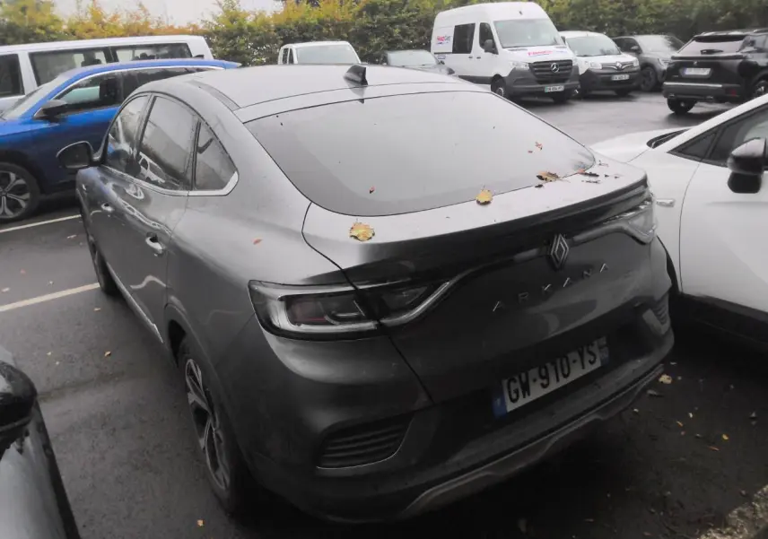 Vue 3/4 arrière d'un Renault Arkana gris métal foncé avec toit ouvrant, garé en extérieur sous un ciel couvert.