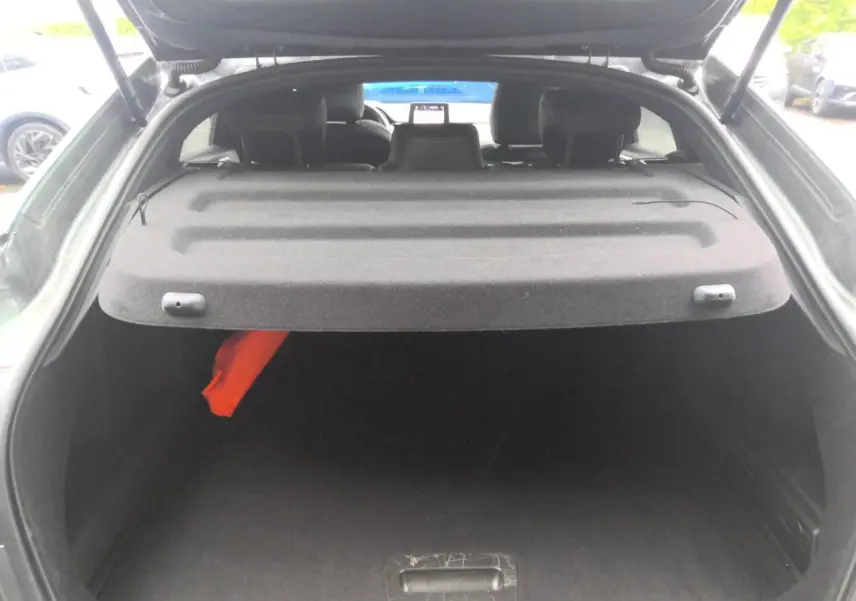 Coffre ouvert vu de l'arrière du Renault Arkana gris métal foncé, avec cache-bagages et intérieur sombre.