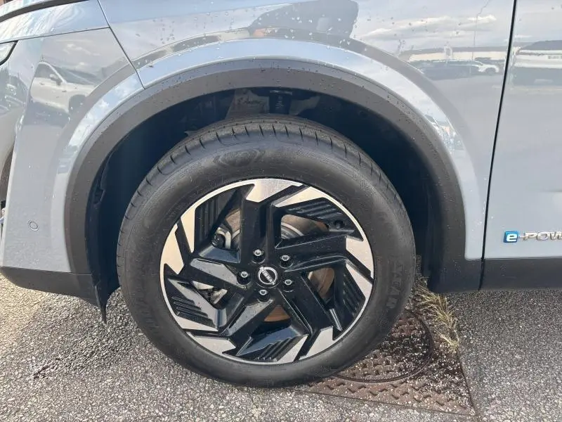 Gros plan sur la roue avant gauche du Nissan Qashqai e-POWER gris Argile avec jante alliage noire et argentée.