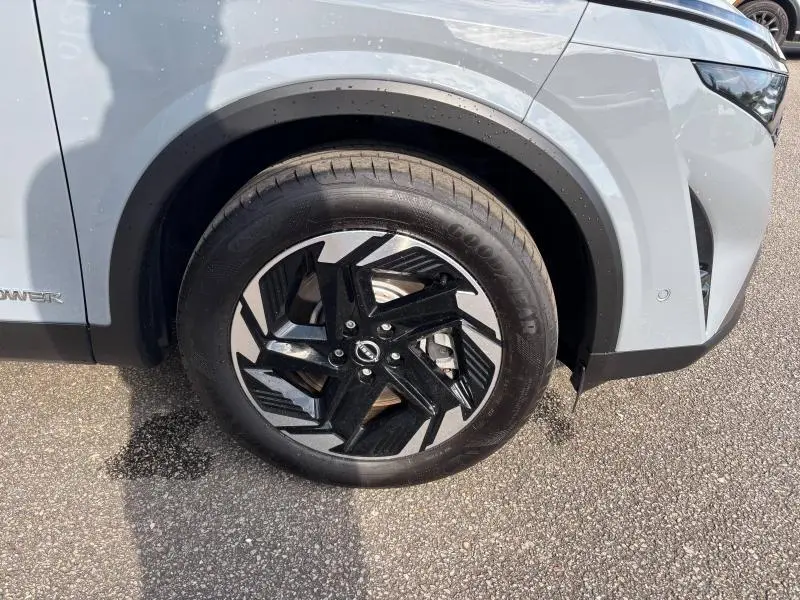 Gros plan sur la roue avant gauche du Nissan Qashqai e-POWER gris Argile avec jante alliage noire et argentée au design moderne.