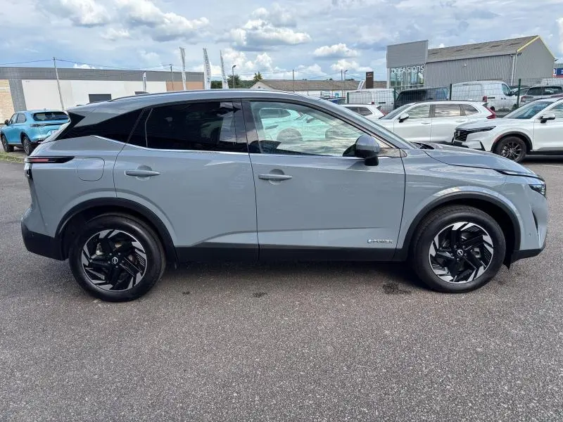 Vue de profil côté gauche d'un Nissan Qashqai e-POWER 2024 en gris Argile avec jantes alliage noires et vitres teintées.