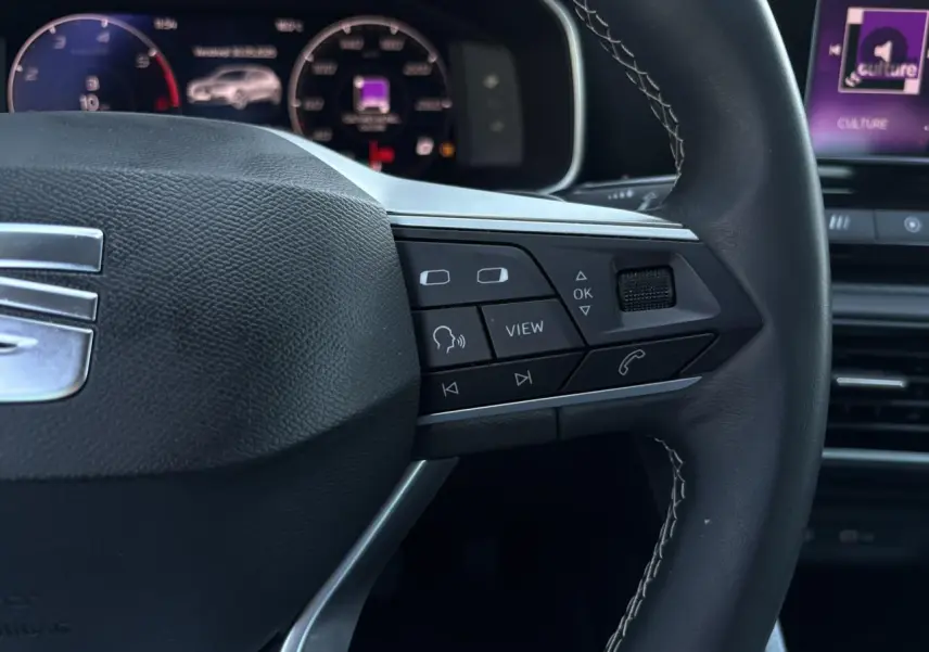 Gros plan sur le volant cuir multifonction de la SEAT LEON 2024 avec commandes intégrées et tableau de bord numérique en arrière-plan