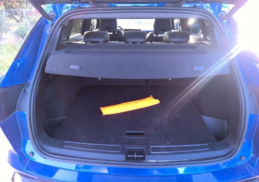Coffre ouvert d'un Renault Austral bleu métal foncé, avec cache-bagages et un objet orange posé à l'intérieur.