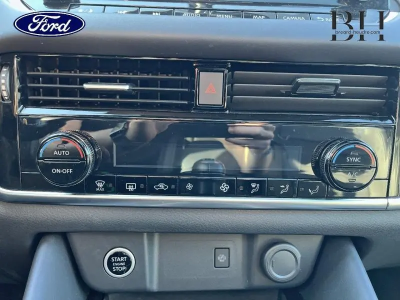 Tableau de bord noir brillant avec commandes climatisation et bouton démarrage d'un Nissan Qashqai Gris Argile, vue frontale rapprochée.