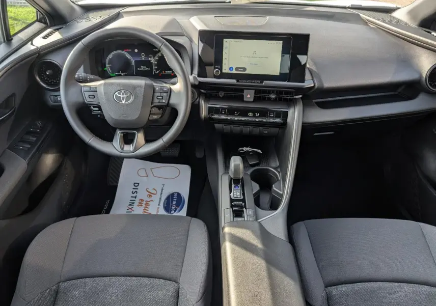 Vue intérieure avant du Toyota C-HR 2024, tableau de bord avec écran tactile 8 pouces et volant multifonction en tissu gris.