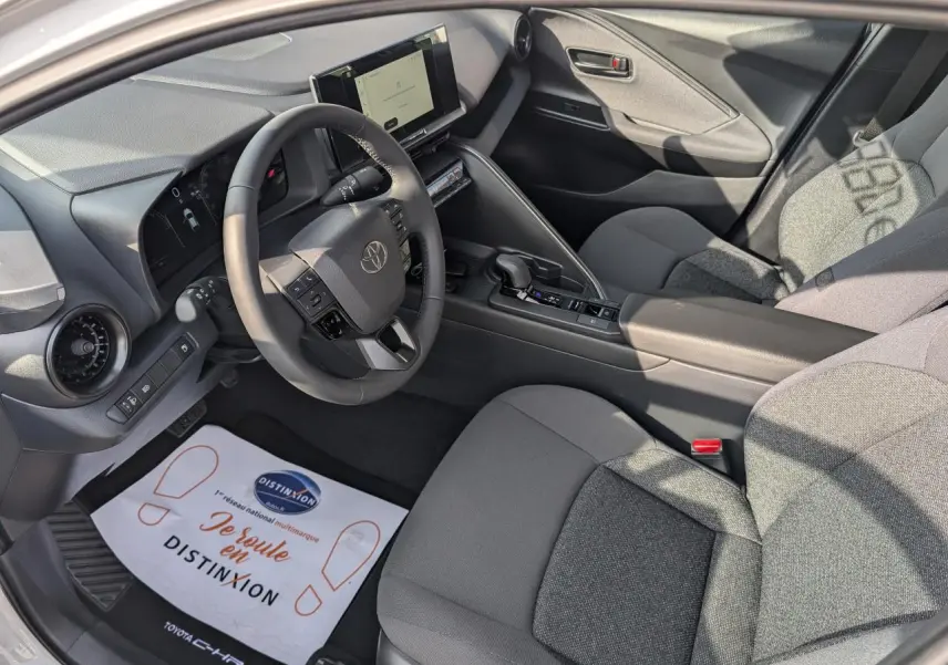 Vue intérieure côté conducteur du Toyota C-HR 2024 hybride, sellerie tissu gris foncé et écran tactile 8 pouces.
