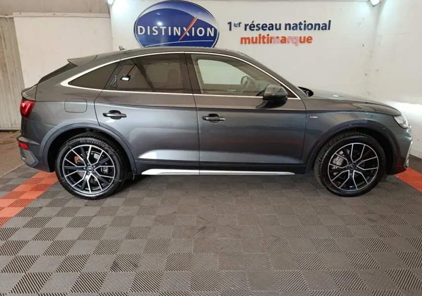 Vue de profil côté droit d'un Audi Q5 gris clair hybride rechargeable 2023 avec jantes noires sport et toit incliné.