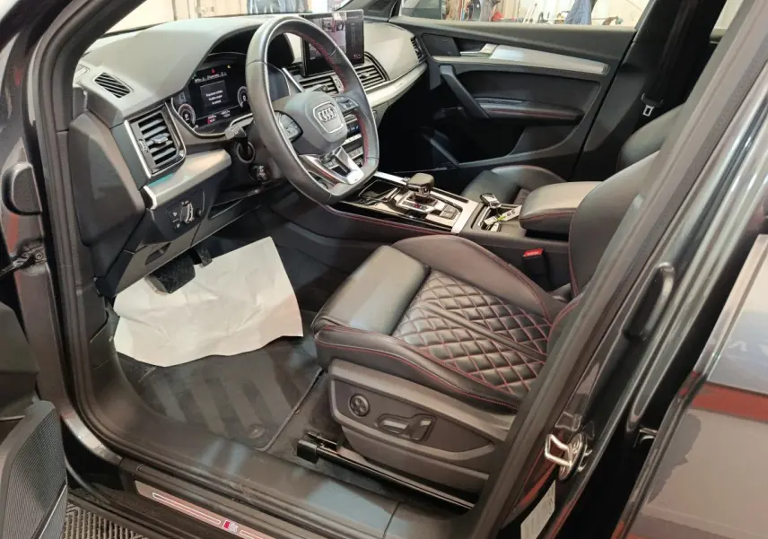 Vue intérieure côté conducteur de l'Audi Q5 2023 gris clair, avec sièges cuir matelassé et volant multifonction.