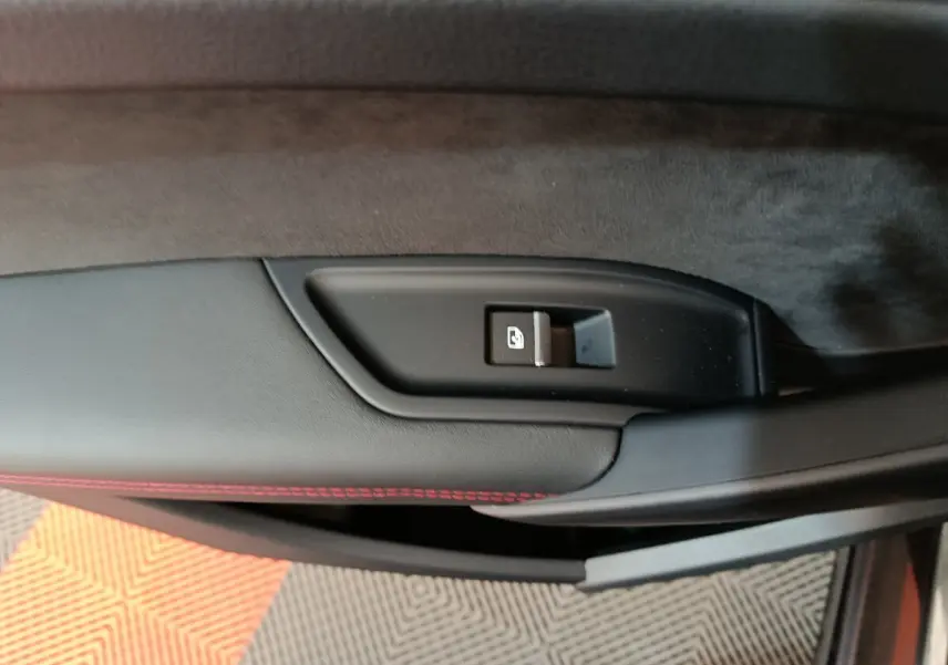 Gros plan sur la commande de verrouillage de porte côté gauche d’un Audi Q5 2023 gris clair avec surpiqûres rouges.