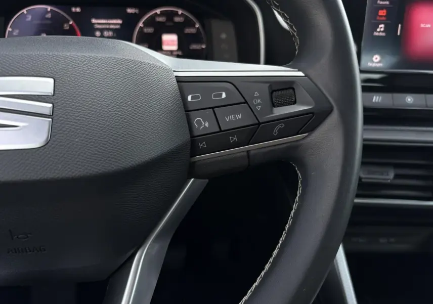 Gros plan sur le volant cuir multifonction de la SEAT LEON 2024 avec commandes intégrées et tableau de bord numérique en arrière-plan.