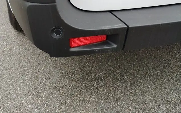 Gros plan sur le coin arrière droit du pare-chocs noir du Nissan Interstar blanc, avec un feu réflecteur rouge intégré.