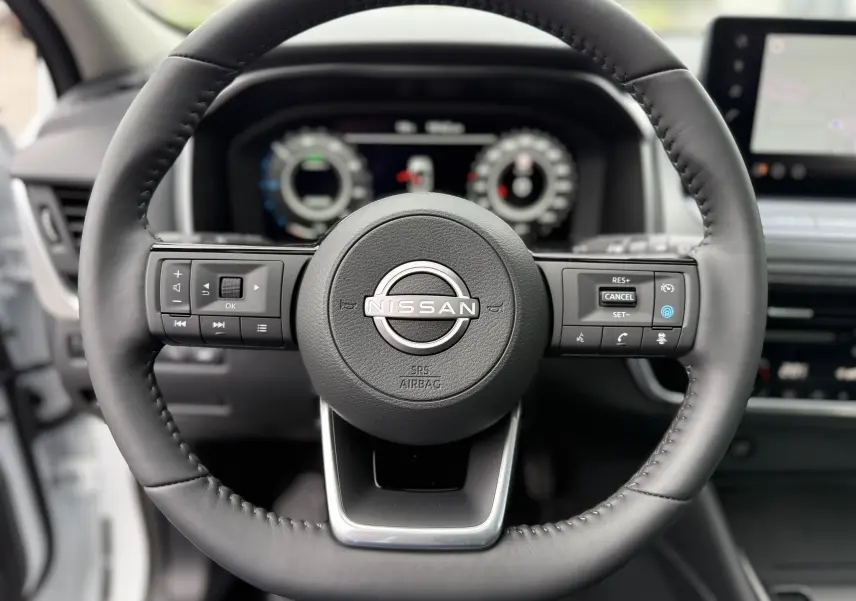 Volant en cuir noir du Nissan Qashqai 2025 avec commandes intégrées et tableau de bord numérique en arrière-plan.