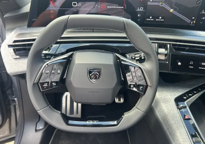 Vue rapprochée du volant GT du Peugeot 5008 Hybrid 145 gris artense, avec tableau de bord numérique et commandes intégrées.