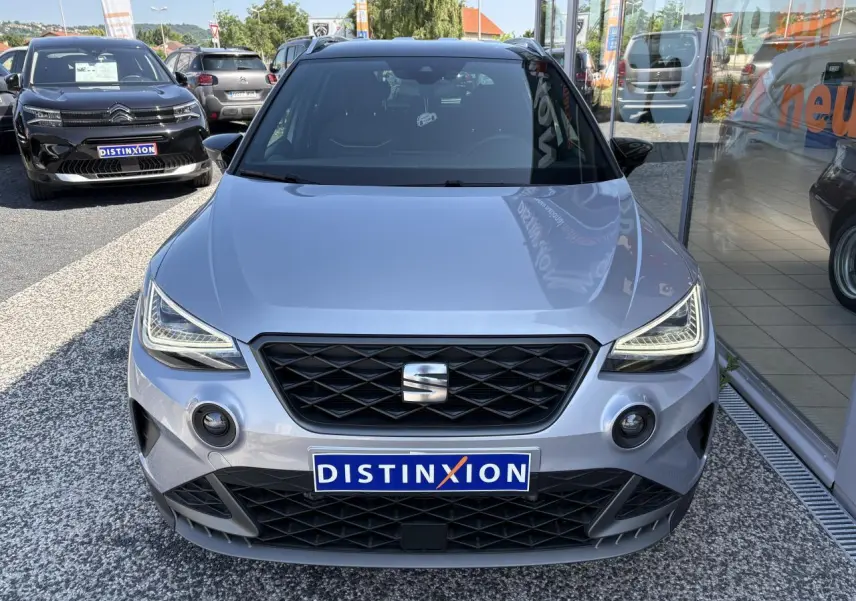 Vue de face d'une SEAT Arona 2024 gris clair avec calandre noire et phares LED au design anguleux.
