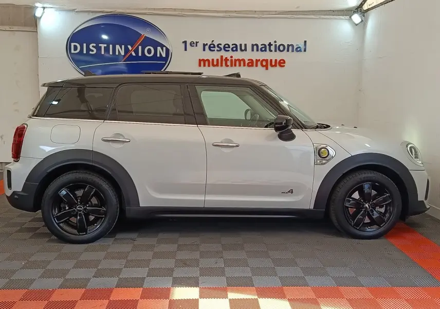 Vue de profil côté gauche d'une MINI Countryman Cooper SE hybride rechargeable blanche avec toit noir et jantes noires.