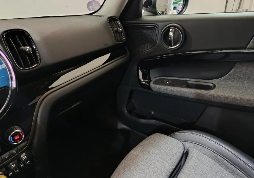 Intérieur côté passager du MINI Countryman blanc, montrant la porte avec garniture grise et tableau de bord noir brillant.