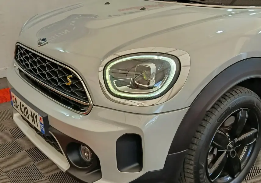 Vue 3/4 avant droit d'une MINI Countryman blanche avec phares LED allumés et jantes noires brillantes.