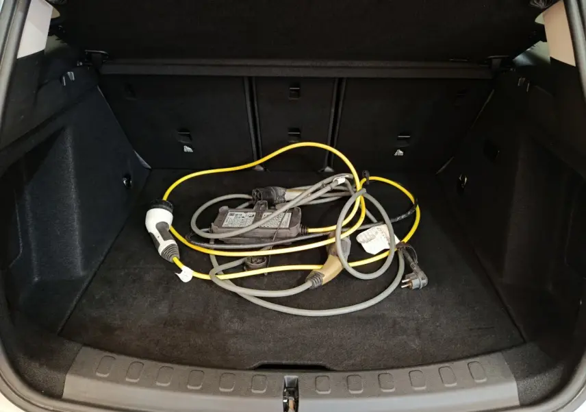 Coffre ouvert d'une MINI Countryman blanc, vue arrière, avec câble de recharge hybride posé au sol.