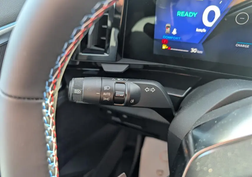 Gros plan sur la commande de clignotants du Renault Austral gris, volant avec surpiqûres tricolores et tableau de bord numérique.