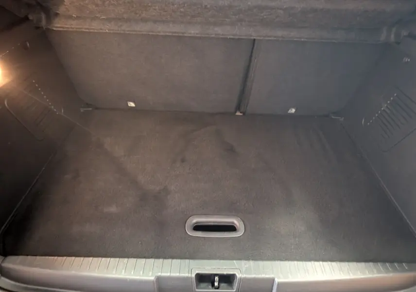 Coffre vide vu de l'arrière d'un Renault Captur gris clair, montrant la moquette noire et les parois latérales.