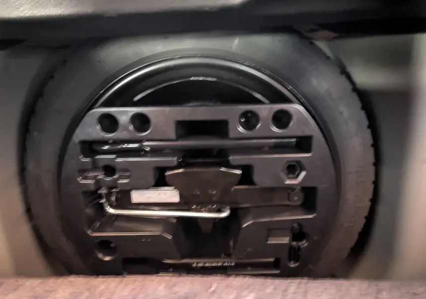 Gros plan sur la roue de secours et son kit d'outils rangés dans le coffre d'un Renault Captur gris clair 2017.