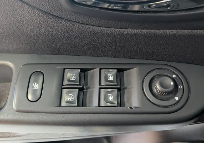 Gros plan sur les commandes de lève-vitres et réglage des rétroviseurs côté conducteur d’un Renault Captur gris clair.