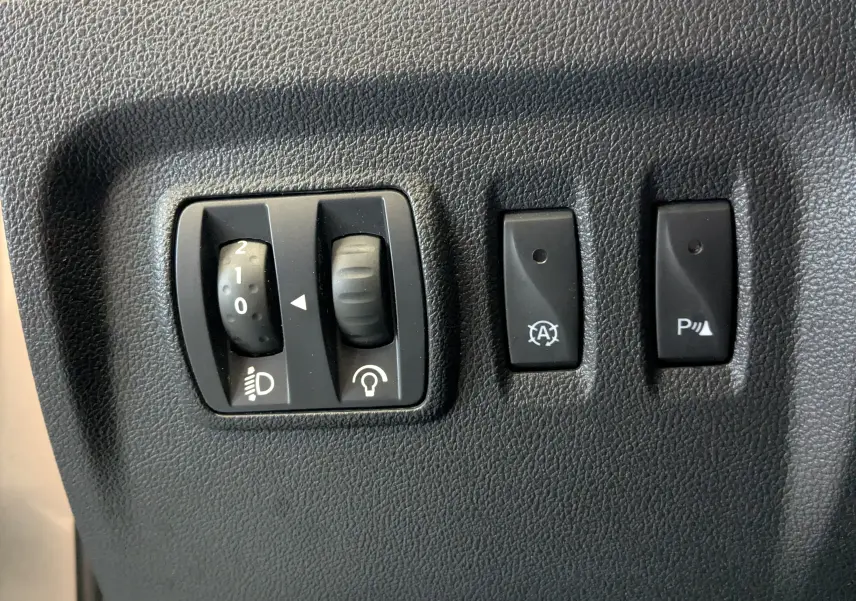 Gros plan sur les commandes intérieures noires du Renault Captur 1.5 dCi 90 Business, réglage phares et boutons de fonction.