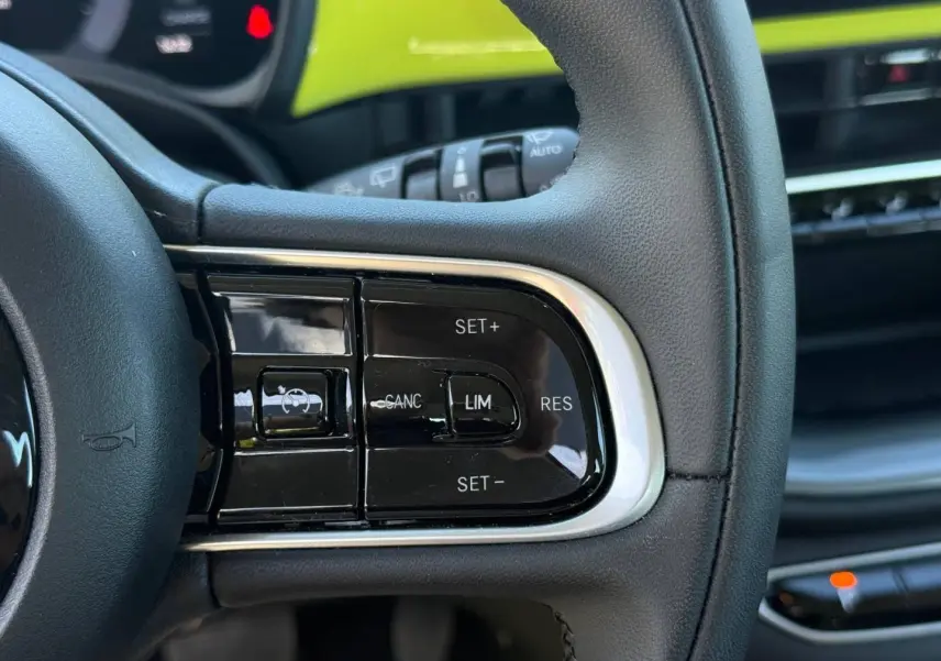 Gros plan sur les commandes de régulateur de vitesse au volant noir du Fiat 500 e jaune, intérieur moderne et épuré.