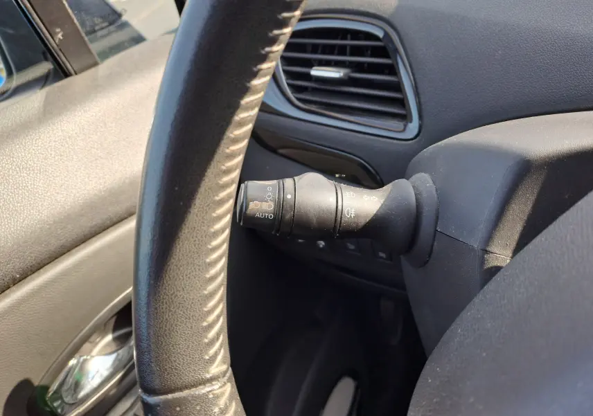 Gros plan sur la manette d'éclairage à gauche du volant dans l'habitacle noir du Renault Scenic III gris 2016.