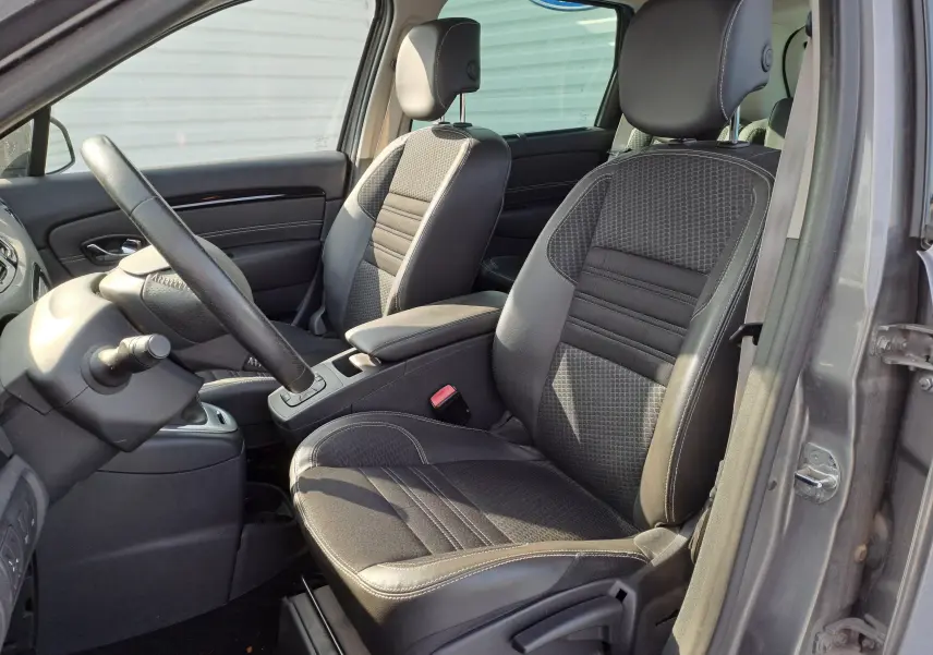 Vue intérieure côté conducteur du Renault Scenic III gris, mettant en valeur les sièges en tissu noir avec surpiqûres et le volant.