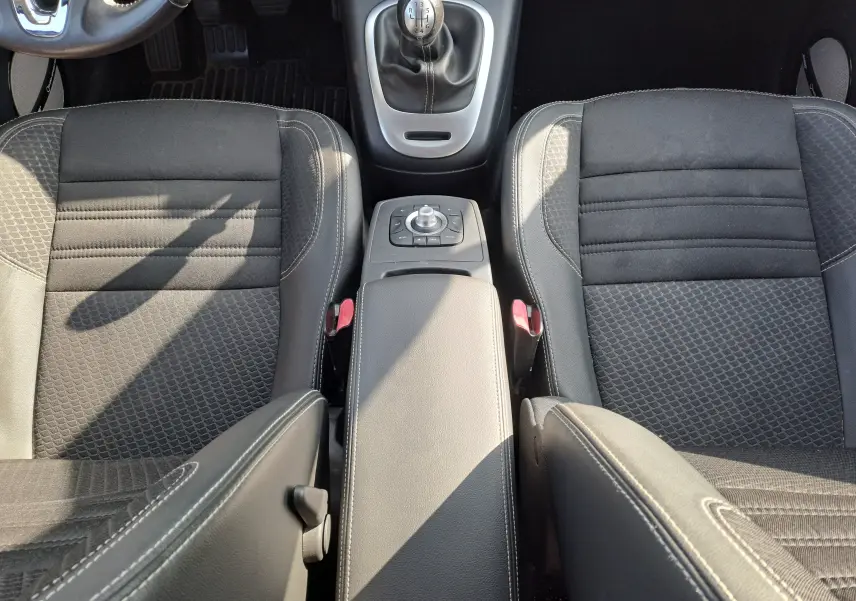 Vue intérieure centrée sur les sièges avant noirs en tissu et cuir, avec levier de vitesse manuel et console centrale du Renault Scenic III gris.