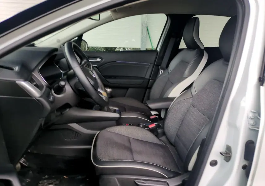 Vue intérieure côté gauche du Renault Captur blanc 2024, montrant les sièges avant bicolores et le volant.