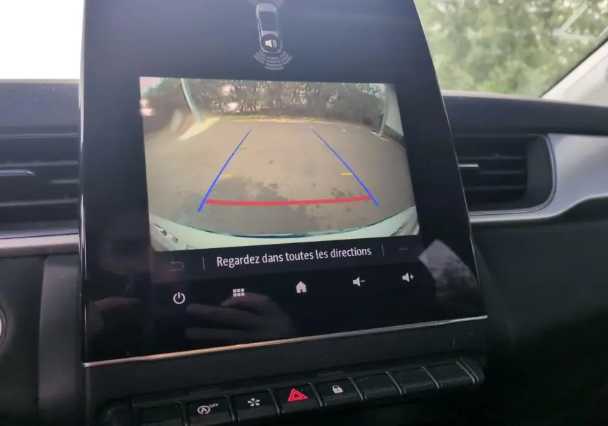 Vue intérieure du tableau de bord du Renault Captur blanc 2024 avec écran de caméra de recul affichant l'aide au stationnement.