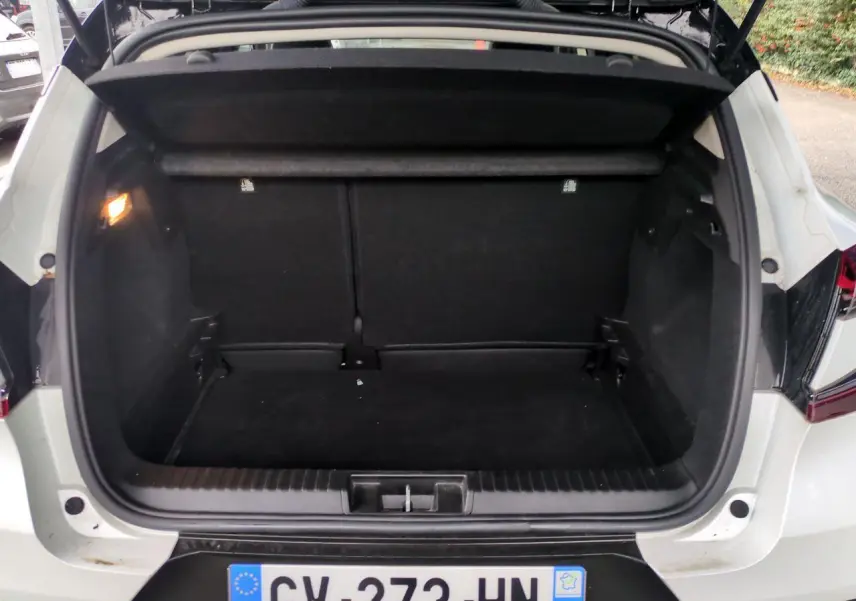 Coffre ouvert vu de l'arrière d'un Renault Captur blanc 2024, avec intérieur de coffre noir et éclairage latéral.