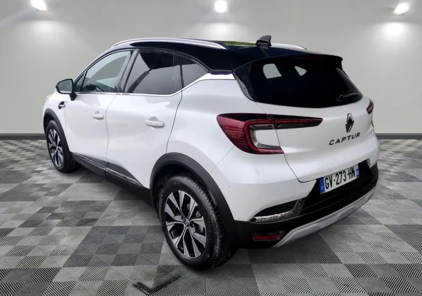 Vue 3/4 arrière droite du Renault Captur blanc avec toit noir et jantes alliage bicolores sur sol carrelé.