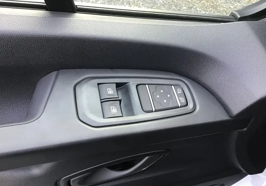 Gros plan sur les commandes de lève-vitres et réglage des rétroviseurs côté gauche du Renault Trafic Fourgon blanc 2025.
