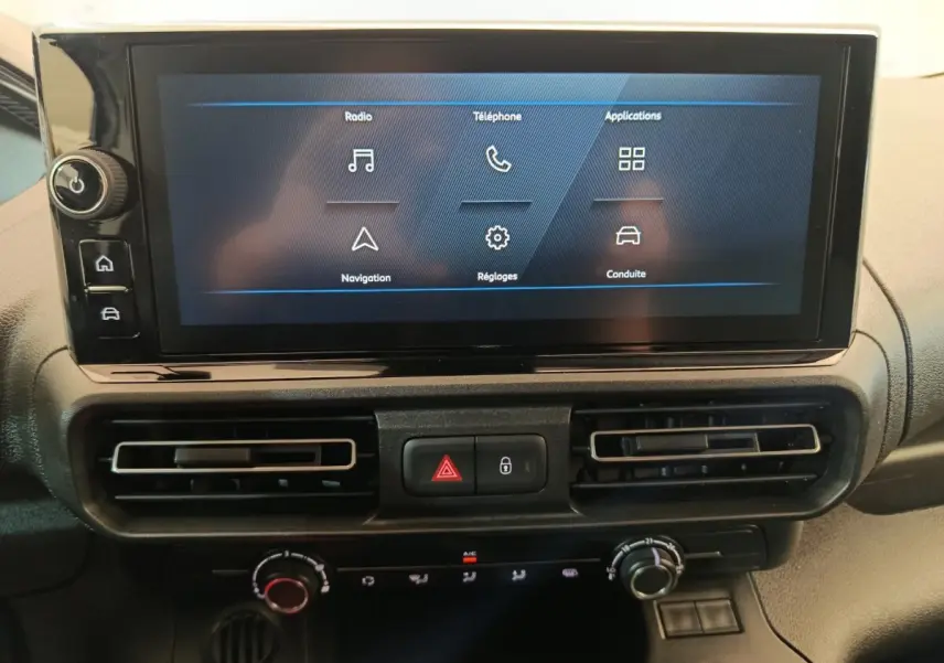 Écran tactile central du Peugeot Partner 2025 avec commandes climatisation et boutons d’alerte, vue de face.