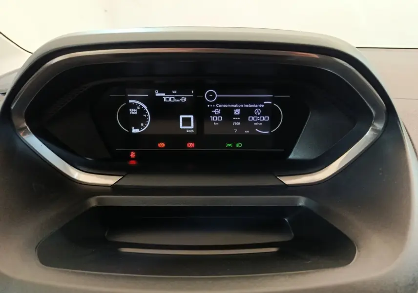 Vue rapprochée du tableau de bord numérique du Peugeot Partner blanc 2025, affichant la consommation instantanée et les alertes.