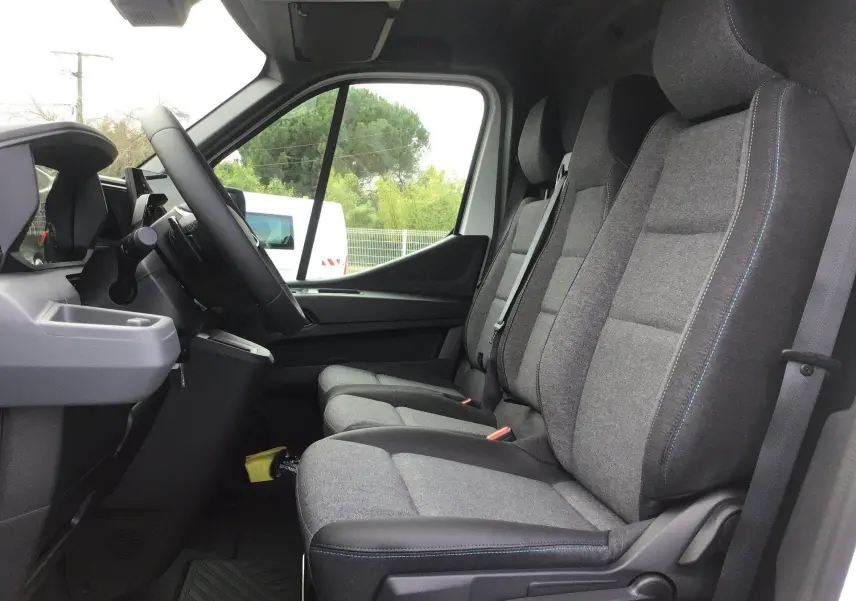 Vue intérieure côté conducteur du Renault Master 2026, montrant les sièges gris avec surpiqûres bleues et tableau de bord noir.