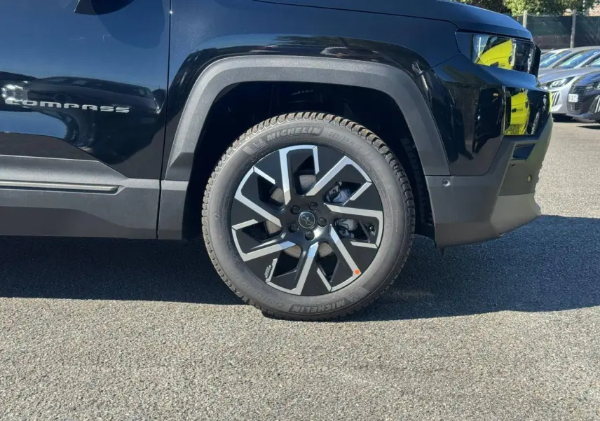 Gros plan sur la roue avant droite noire du Jeep Compass 2026 avec jante alu et logo Jeep visible sur la carrosserie.