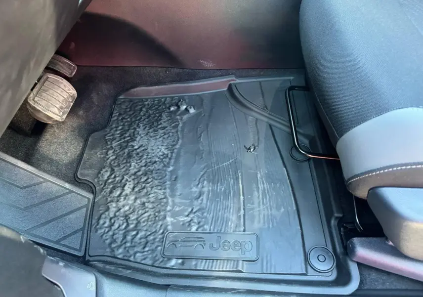 Gros plan sur le tapis de sol noir côté conducteur du Jeep Compass 2026 avec logo Jeep visible au pied du siège gris anthracite.