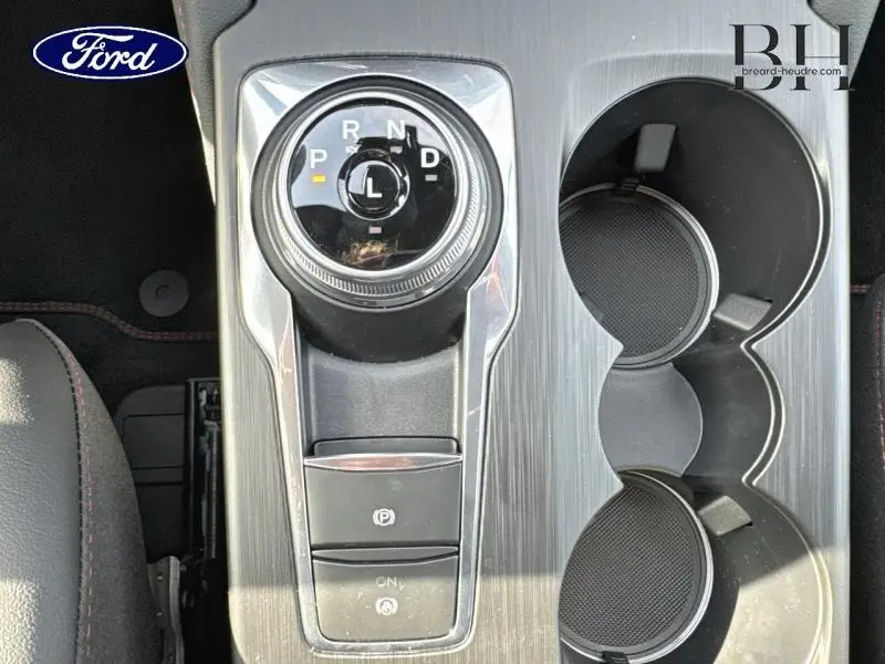 Vue plongeante sur la console centrale grise du Ford Kuga 2025, avec molette de boîte auto et porte-gobelets noirs.