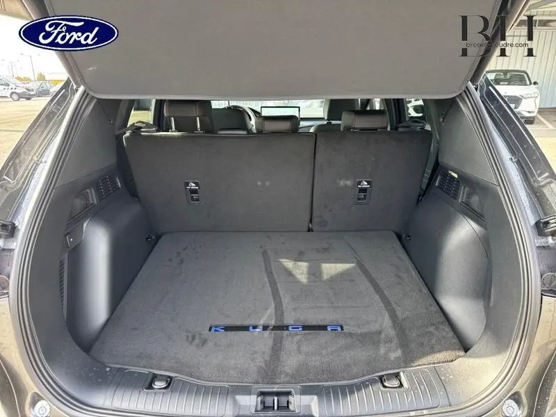 Coffre ouvert d'un Ford Kuga gris Magnetic Fashion, montrant le tapis de coffre avec logo KUGA visible.