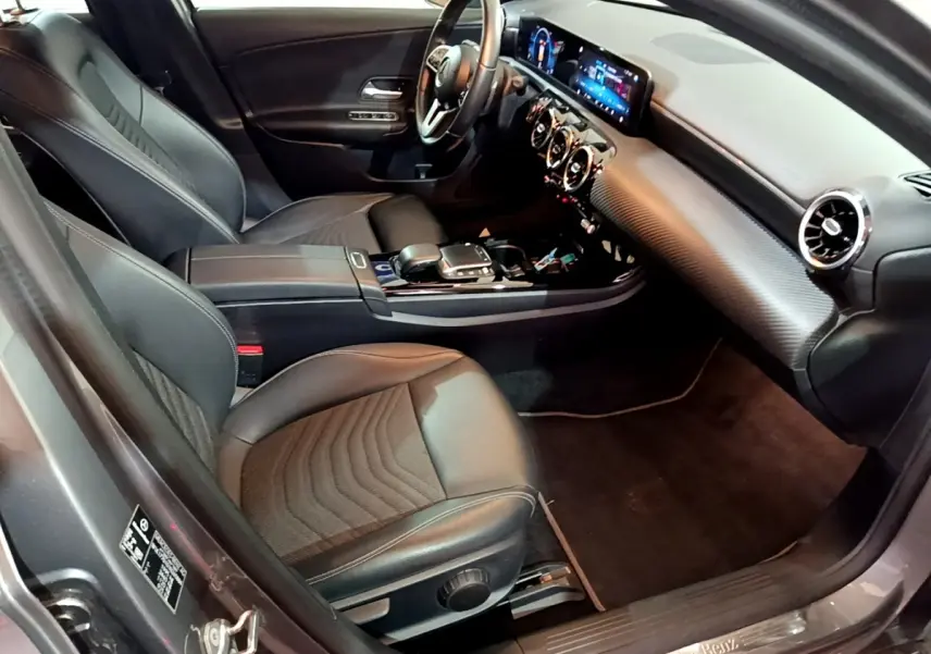 Vue intérieure côté conducteur d'une Mercedes Classe A 180 d Business Line 2021 avec sièges cuir noirs et tableau de bord digital.