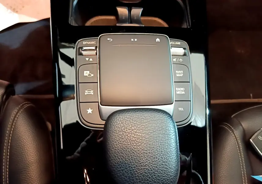Gros plan sur la console centrale noire brillante et le pavé tactile avec repose-poignet cuir dans une Mercedes Classe A gris foncé.