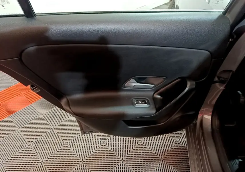 Vue intérieure de la porte arrière droite d'une Mercedes Classe A gris foncé, avec poignée argentée et bouton de vitre électrique.