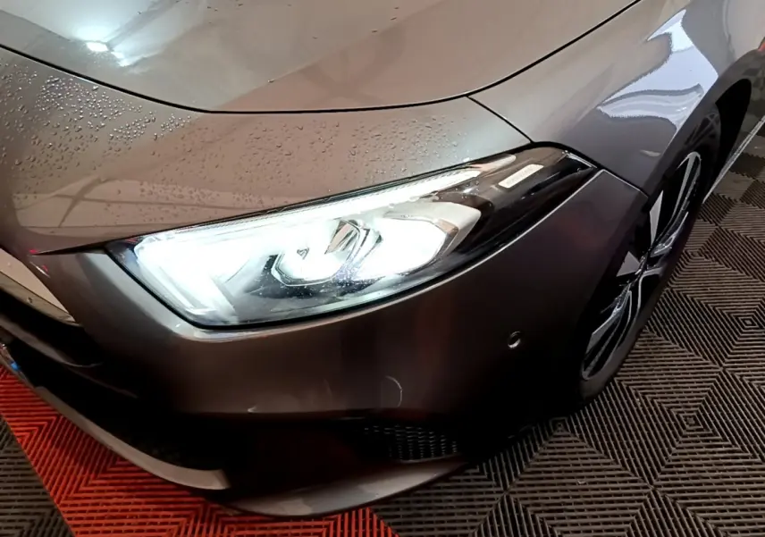 Gros plan sur l'avant droit gris foncé d'une Mercedes Classe A 180 d avec phare LED allumé et jante visible.