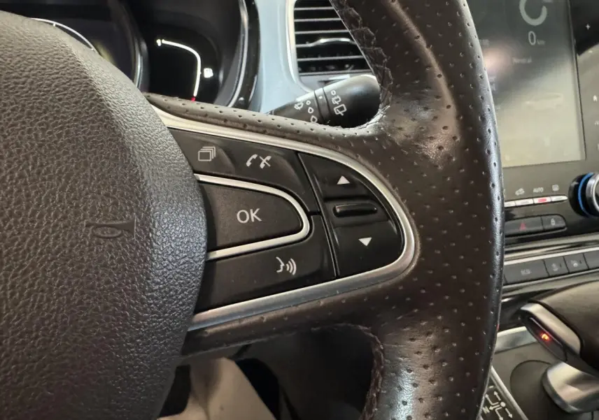 Gros plan sur le volant en cuir noir perforé côté gauche du Renault Espace gris foncé avec commandes multifonctions et écran tactile visible.