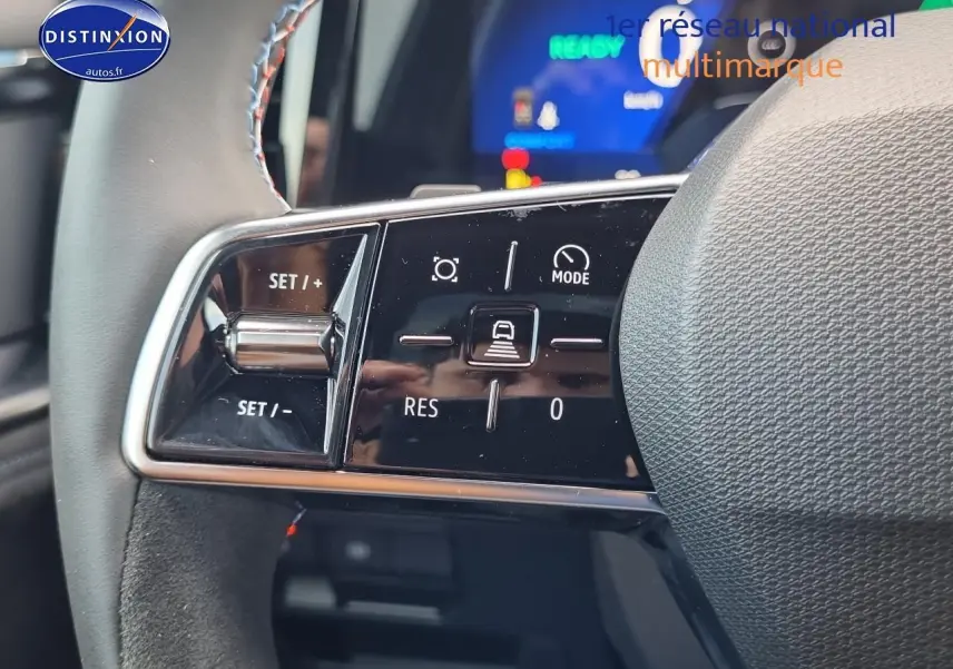 Gros plan sur les commandes du volant gris du Renault Espace VI hybride, avec affichage numérique flou en arrière-plan.